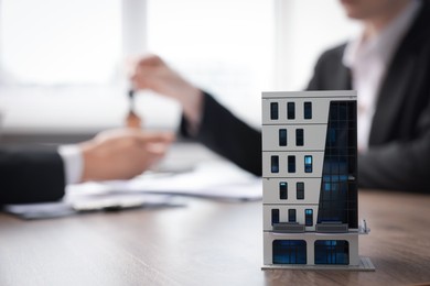 Photo of Real estate agent giving key to client at desk in office, focus on house model
