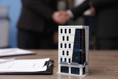 Photo of Real estate agent and client shaking hands in office, focus on house model on desk