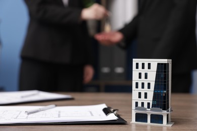 Photo of Real estate agent giving key to client in office, focus on house model on desk