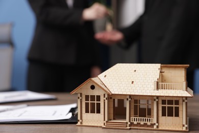 Photo of Real estate agent giving key to client in office, focus on house model on desk