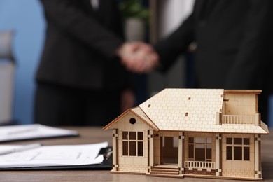 Photo of Real estate agent and client shaking hands in office, focus on house model on desk