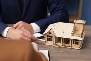 Photo of Real estate agent working with client at desk with house model in office, closeup