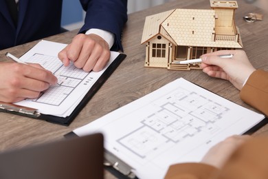 Photo of Real estate agent working with client at desk with house model in office, closeup