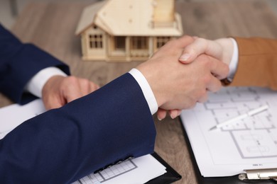 Photo of Real estate agent and client shaking hands at desk with house model in office, closeup