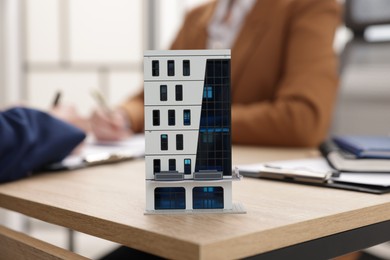 Photo of Real estate agent working with client at desk in office, focus on house model
