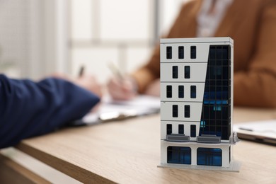 Photo of Real estate agent working with client at desk in office, focus on house model