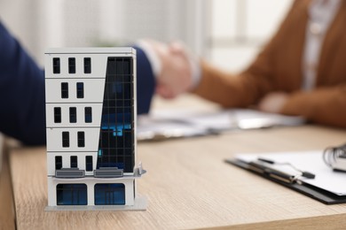 Photo of Real estate agent and client shaking hands at desk in office, focus on house model