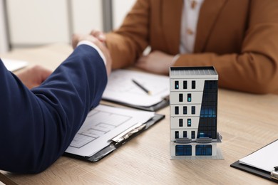 Photo of Real estate agent working with client at desk in office, focus on house model