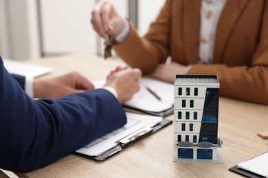 Photo of Real estate agent working with client at desk in office, focus on house model