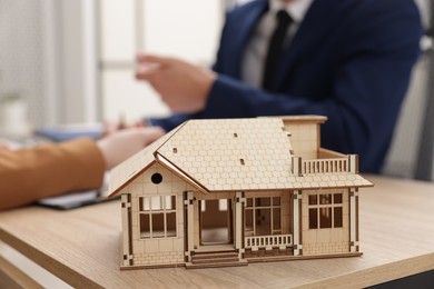 Photo of Real estate agent working with client at desk in office, focus on house model