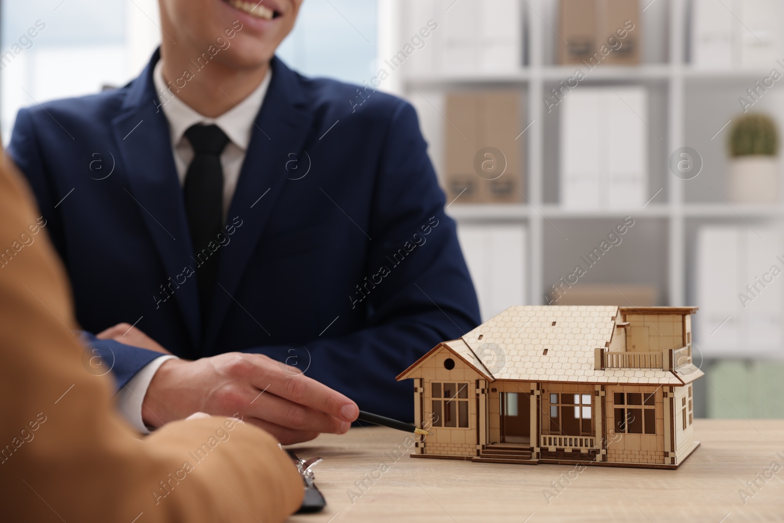 Real estate agent working with client at desk in office, focus on house model Photo of Real estate agent working with client at desk in office, focus on house model