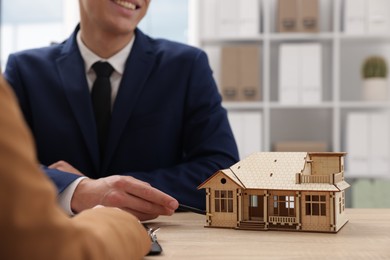 Photo of Real estate agent working with client at desk in office, focus on house model