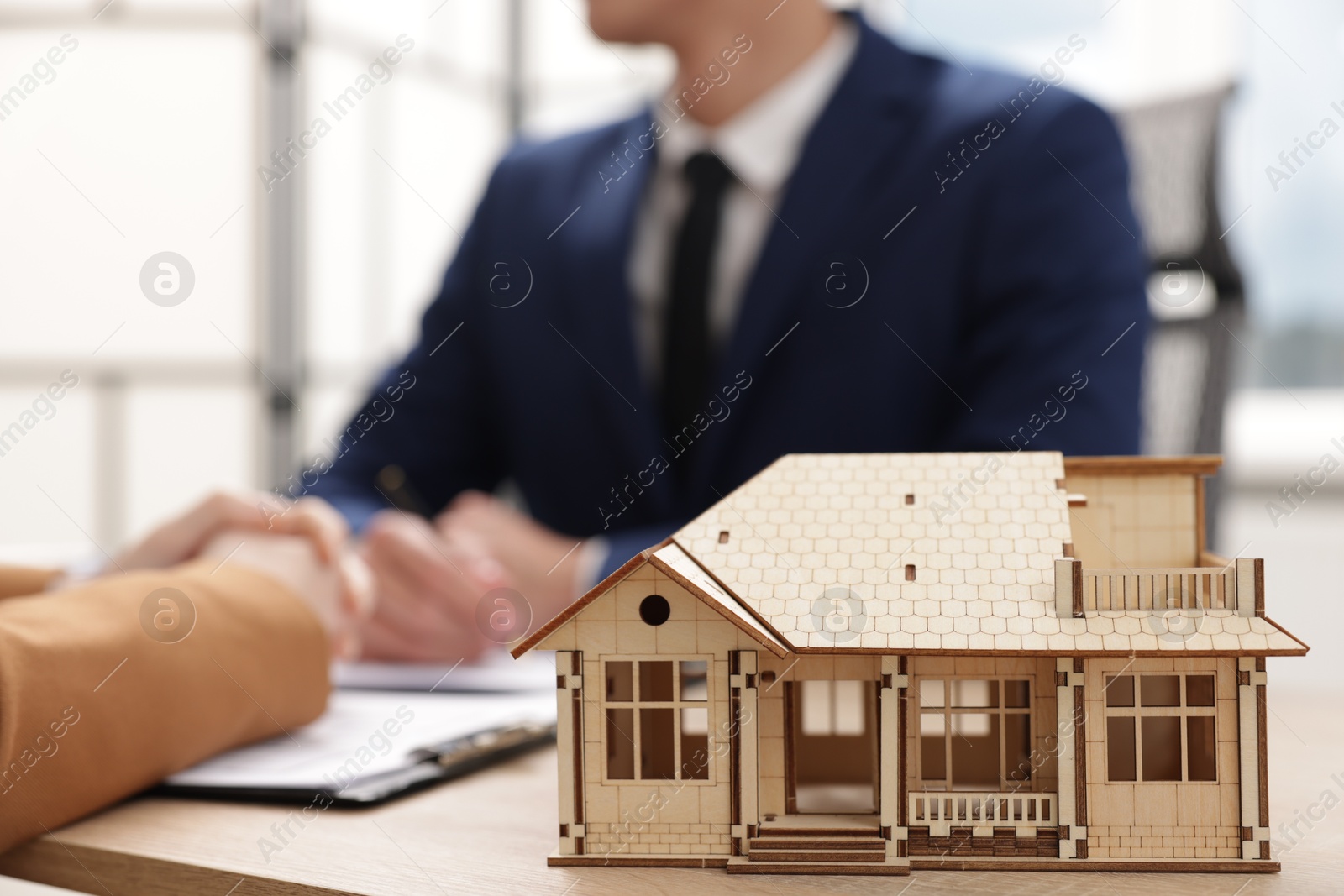 Photo of Real estate agent working with client at desk in office, focus on house model