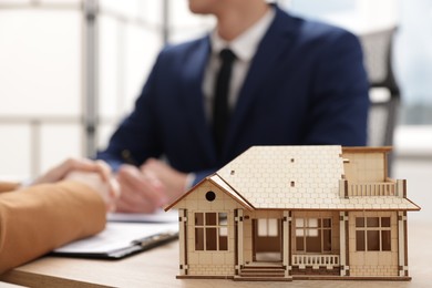 Photo of Real estate agent working with client at desk in office, focus on house model
