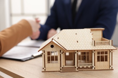 Photo of Real estate agent and client shaking hands at desk in office, focus on house model