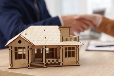 Photo of Real estate agent and client shaking hands at desk in office, focus on house model