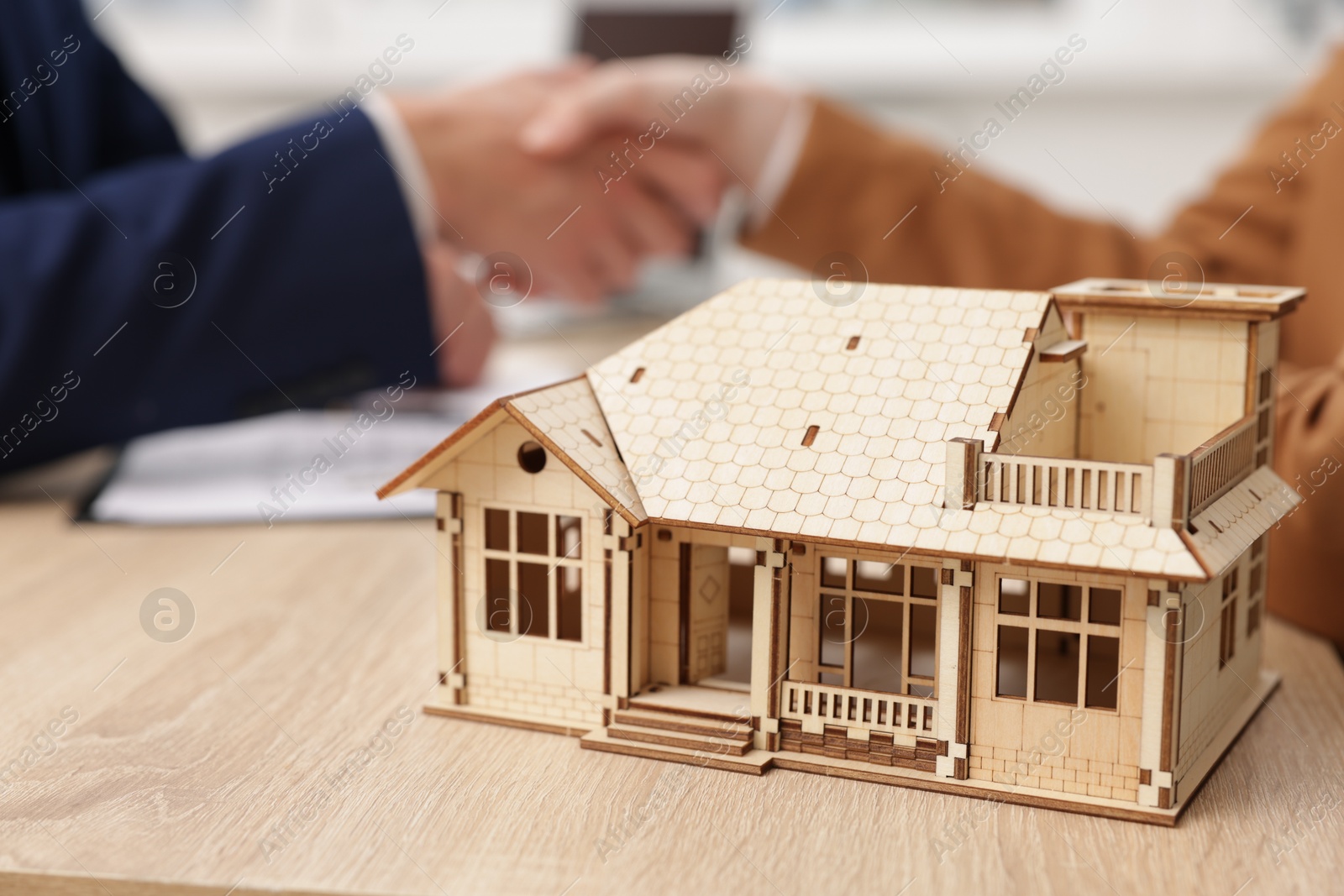 Real estate agent and client shaking hands at desk in office, focus on house model Photo of Real estate agent and client shaking hands at desk in office, focus on house model