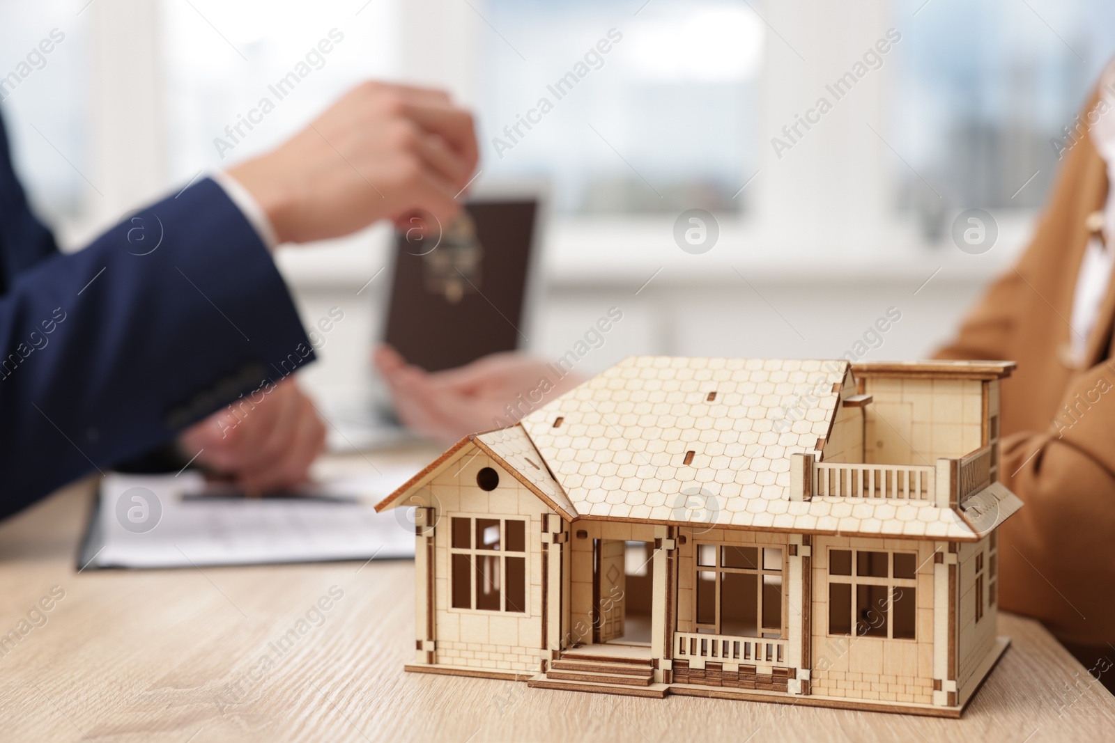 Real estate agent giving key to client at desk in office, focus on house model Photo of Real estate agent giving key to client at desk in office, focus on house model