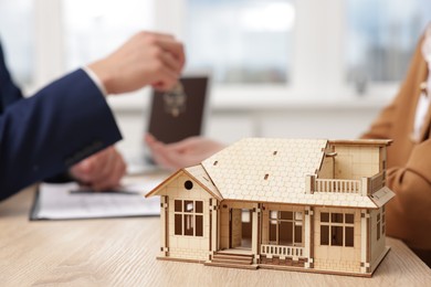 Photo of Real estate agent giving key to client at desk in office, focus on house model