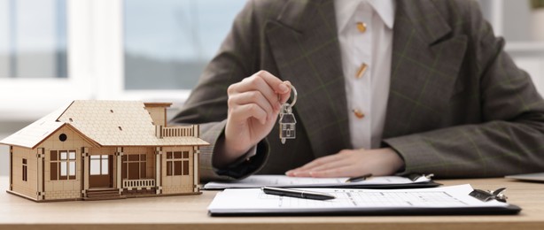 Photo of Real estate agent holding key at desk in office, focus on house model