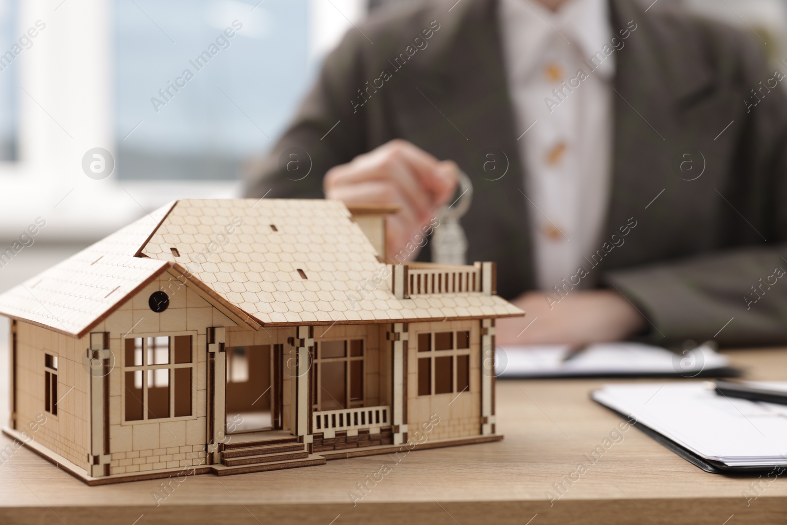 Photo of Real estate agent holding key at desk in office, focus on house model