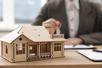 Photo of Real estate agent holding key at desk in office, focus on house model