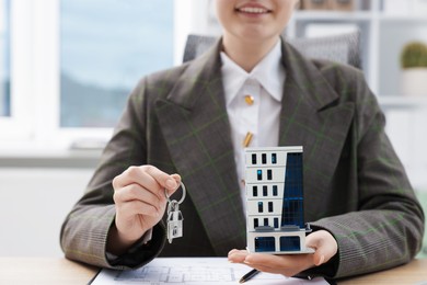 Photo of Real estate agent holding key and house model at desk in office, closeup
