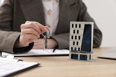Photo of Real estate agent holding key and house model at desk in office, closeup
