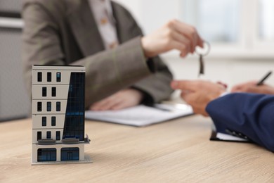 Photo of Real estate agent giving key to client at desk in office, focus on house model