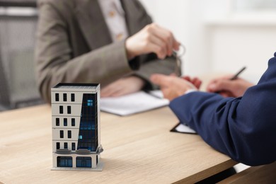 Photo of Real estate agent giving key to client at desk in office, focus on house model