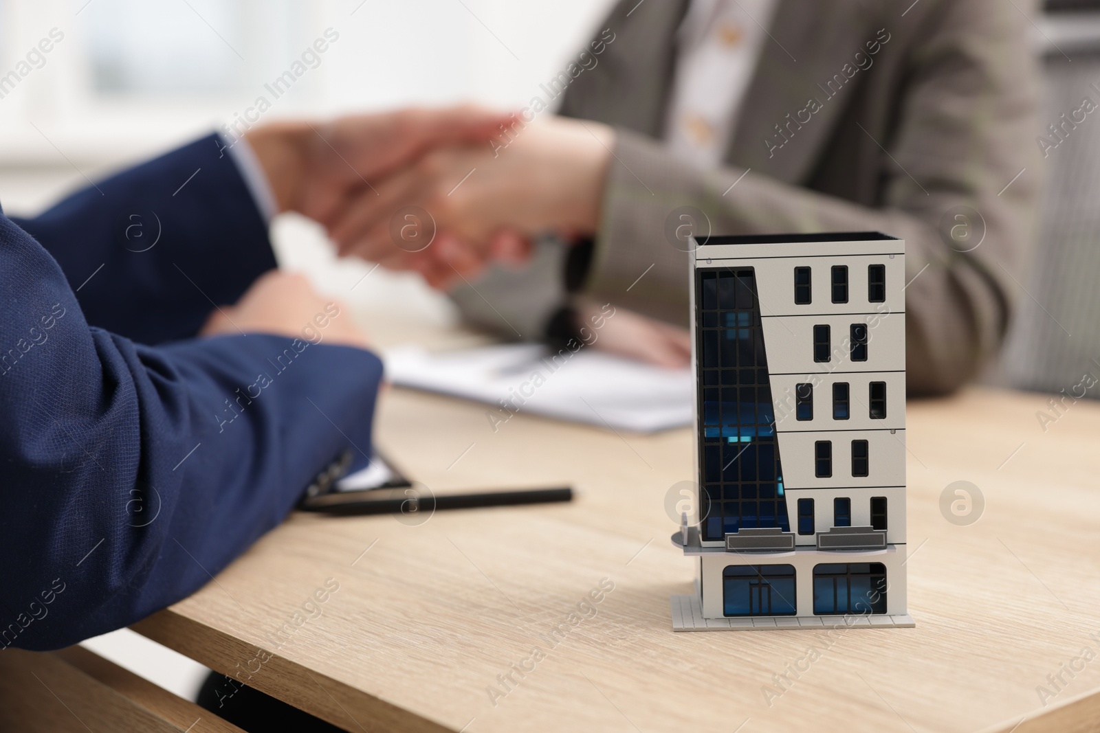 Real estate agent and client shaking hands at desk in office, focus on house model Photo of Real estate agent and client shaking hands at desk in office, focus on house model