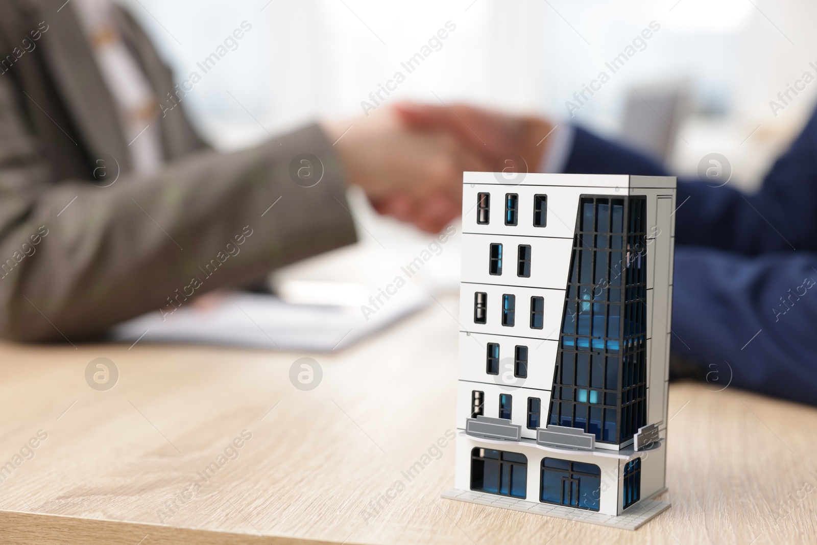 Photo of Real estate agent and client shaking hands at desk in office, focus on house model