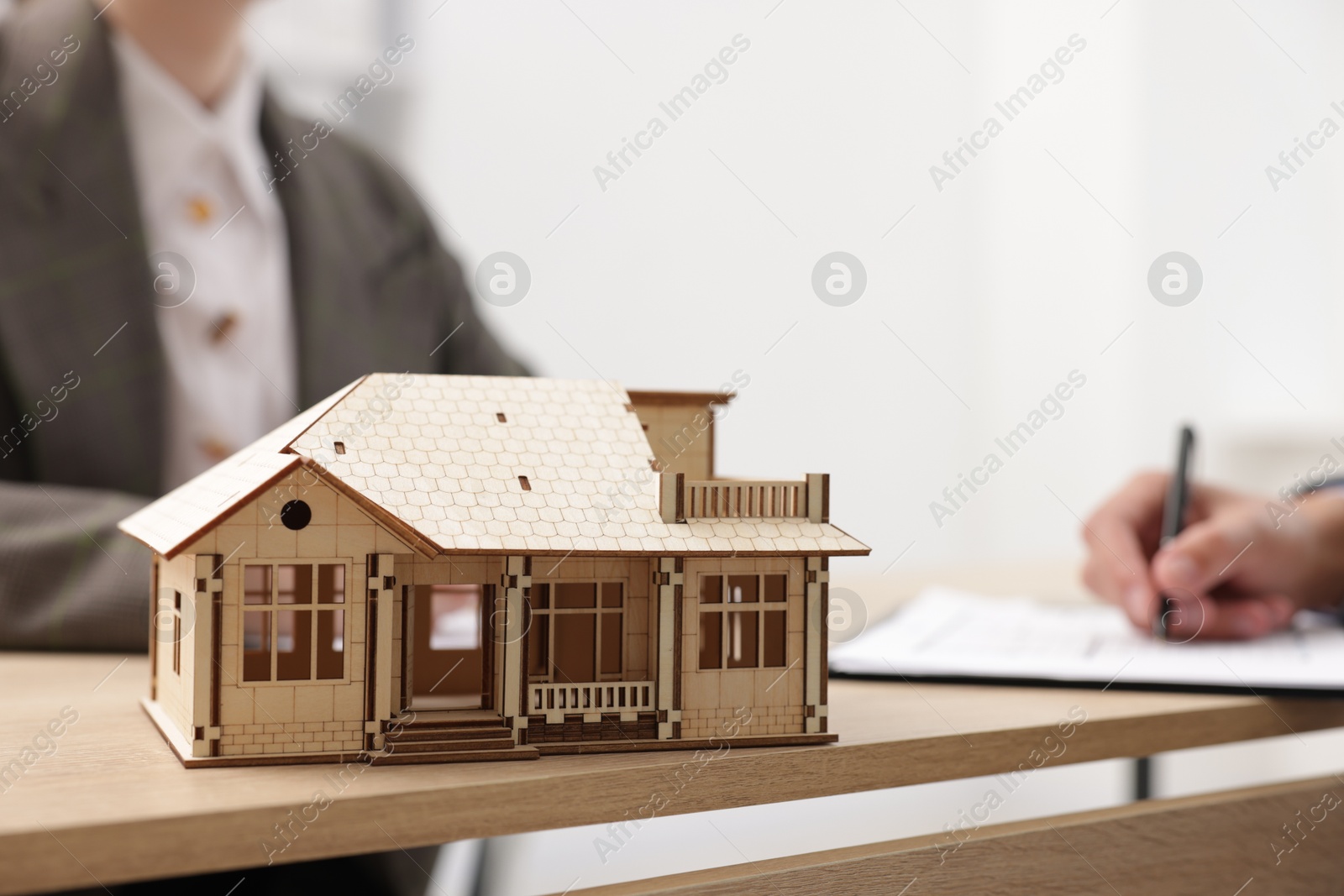 Photo of Real estate agent working with client at desk in office, focus on house model