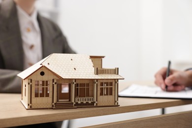 Photo of Real estate agent working with client at desk in office, focus on house model