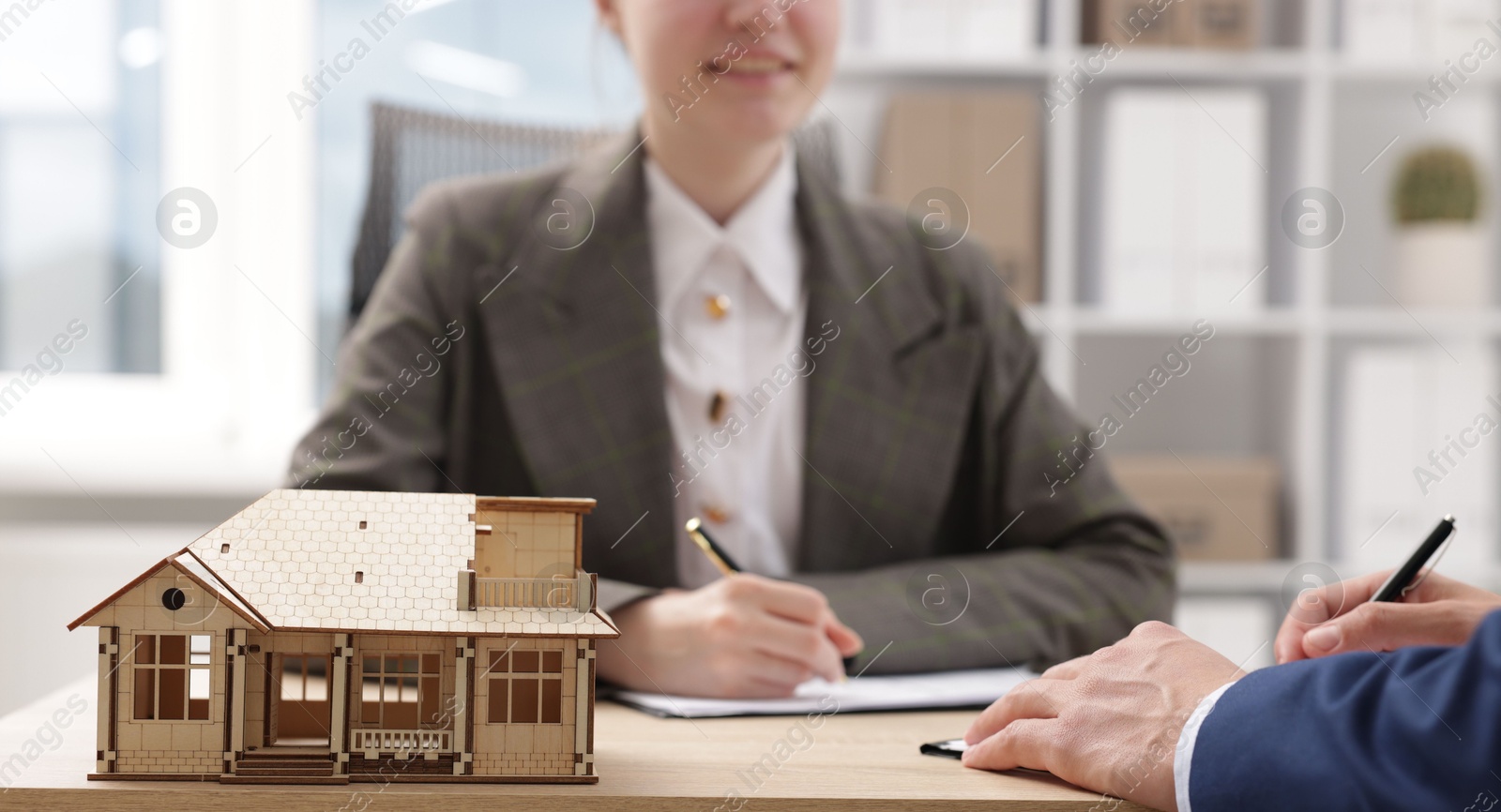 Photo of Real estate agent working with client at desk in office, focus on house model