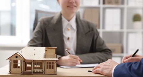 Photo of Real estate agent working with client at desk in office, focus on house model