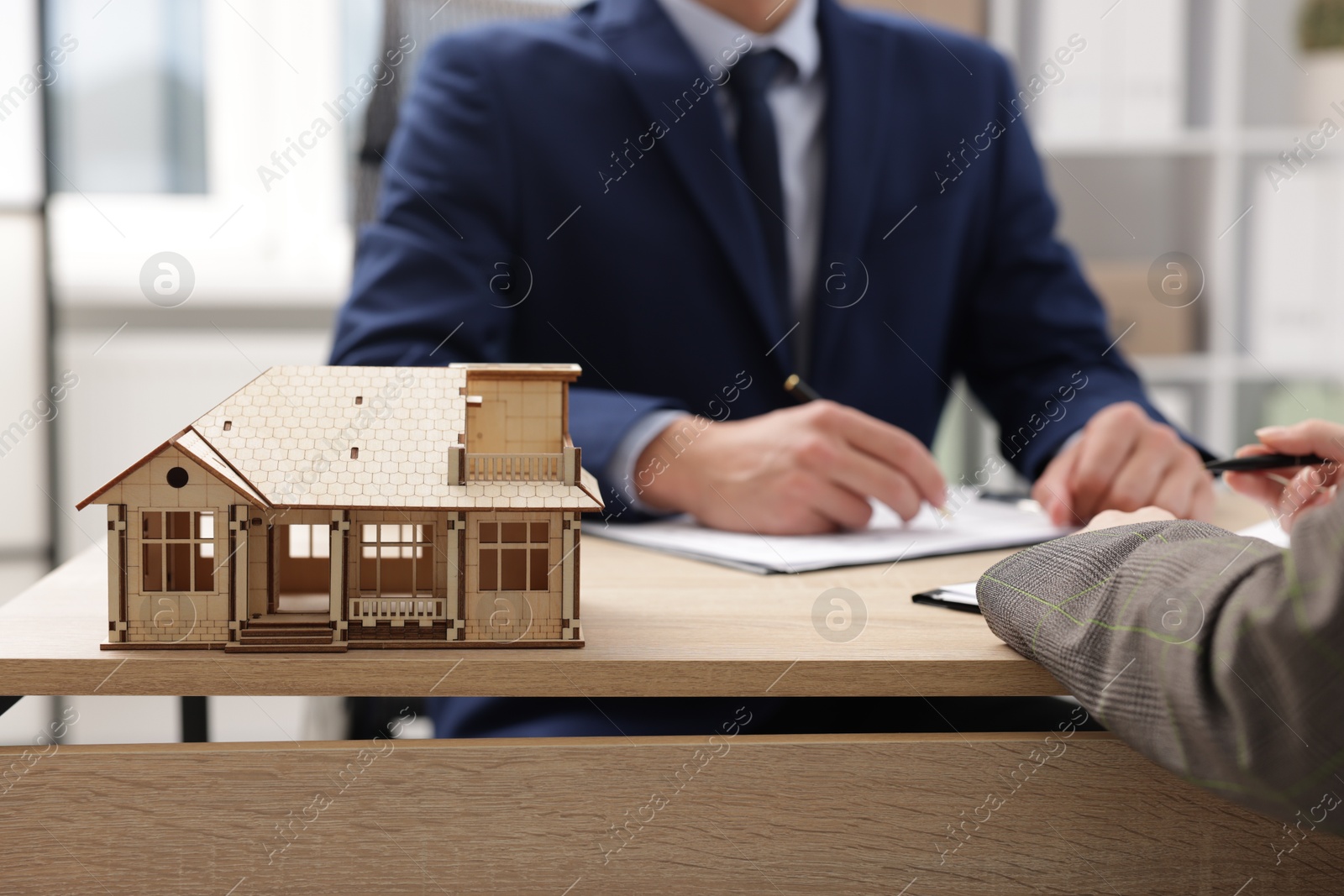 Photo of Real estate agent working with client at desk in office, focus on house model