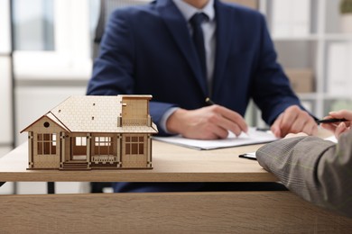 Photo of Real estate agent working with client at desk in office, focus on house model