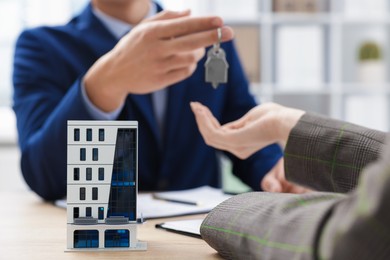 Photo of Real estate agent giving key to client at desk in office, focus on house model