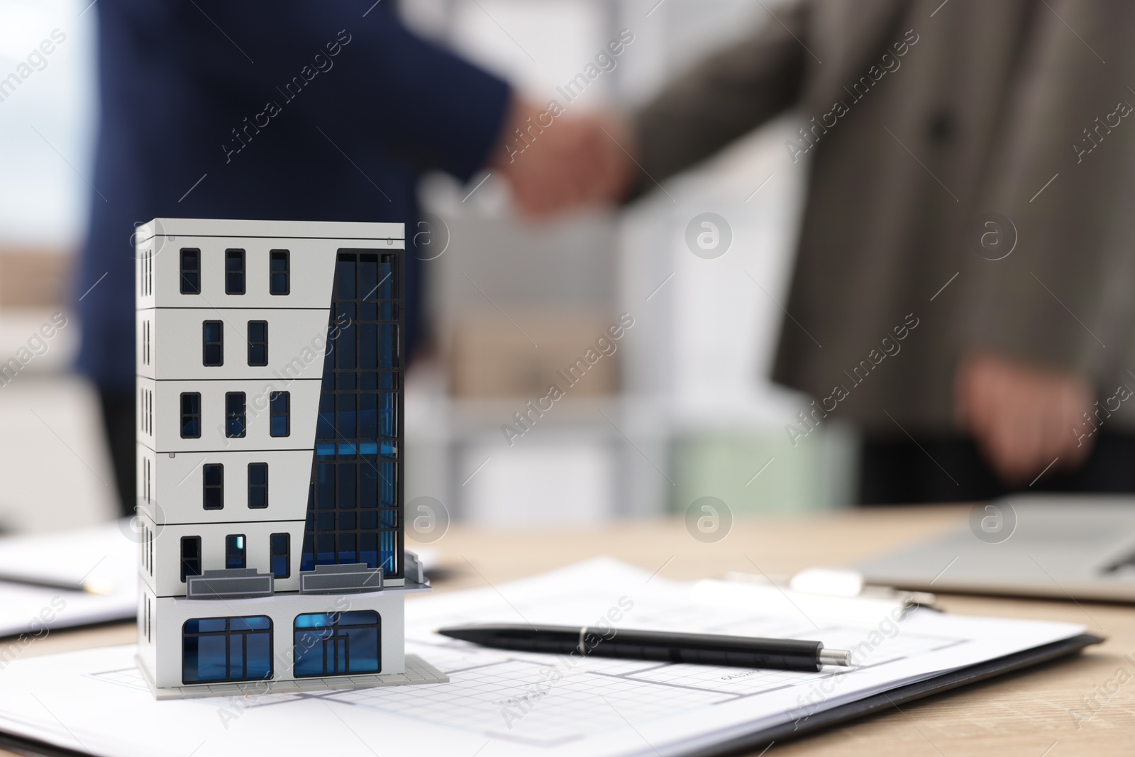 Real estate agent and client shaking hands at desk in office, focus on house model Photo of Real estate agent and client shaking hands at desk in office, focus on house model