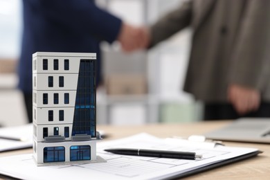Photo of Real estate agent and client shaking hands at desk in office, focus on house model