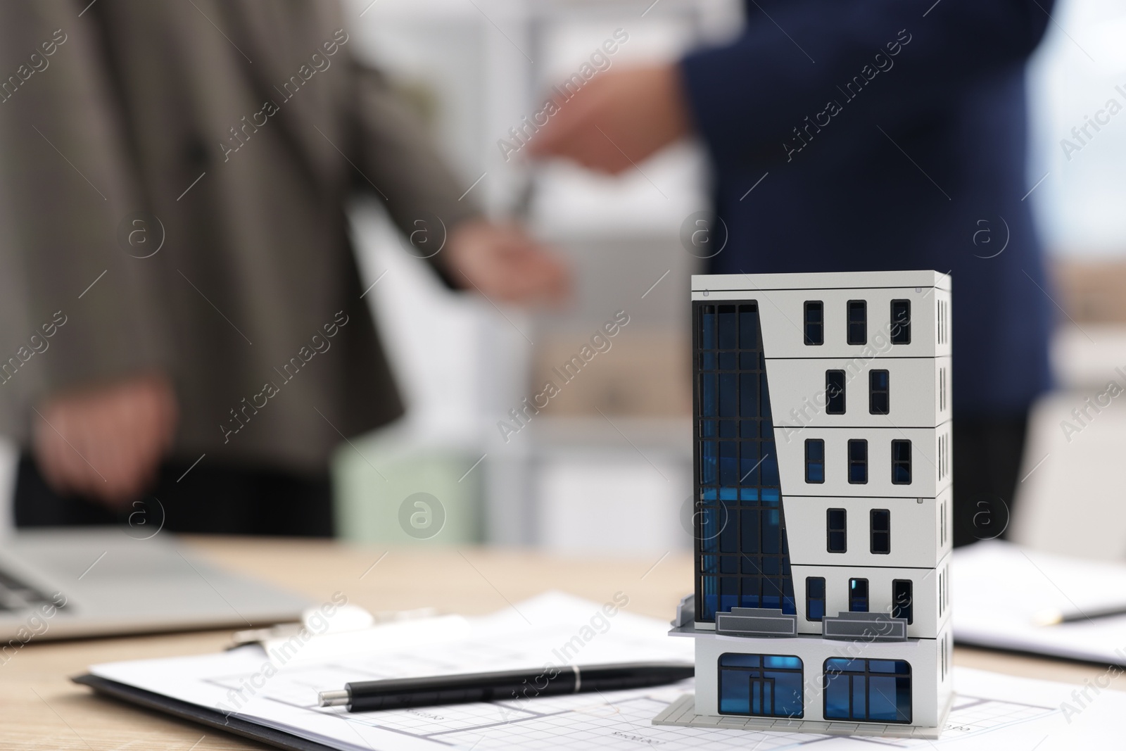 Real estate agent giving key to client at desk in office, focus on house model Photo of Real estate agent giving key to client at desk in office, focus on house model
