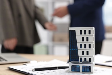 Photo of Real estate agent giving key to client at desk in office, focus on house model