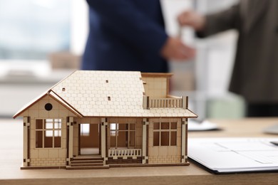 Photo of Real estate agent giving key to client at desk in office, focus on house model