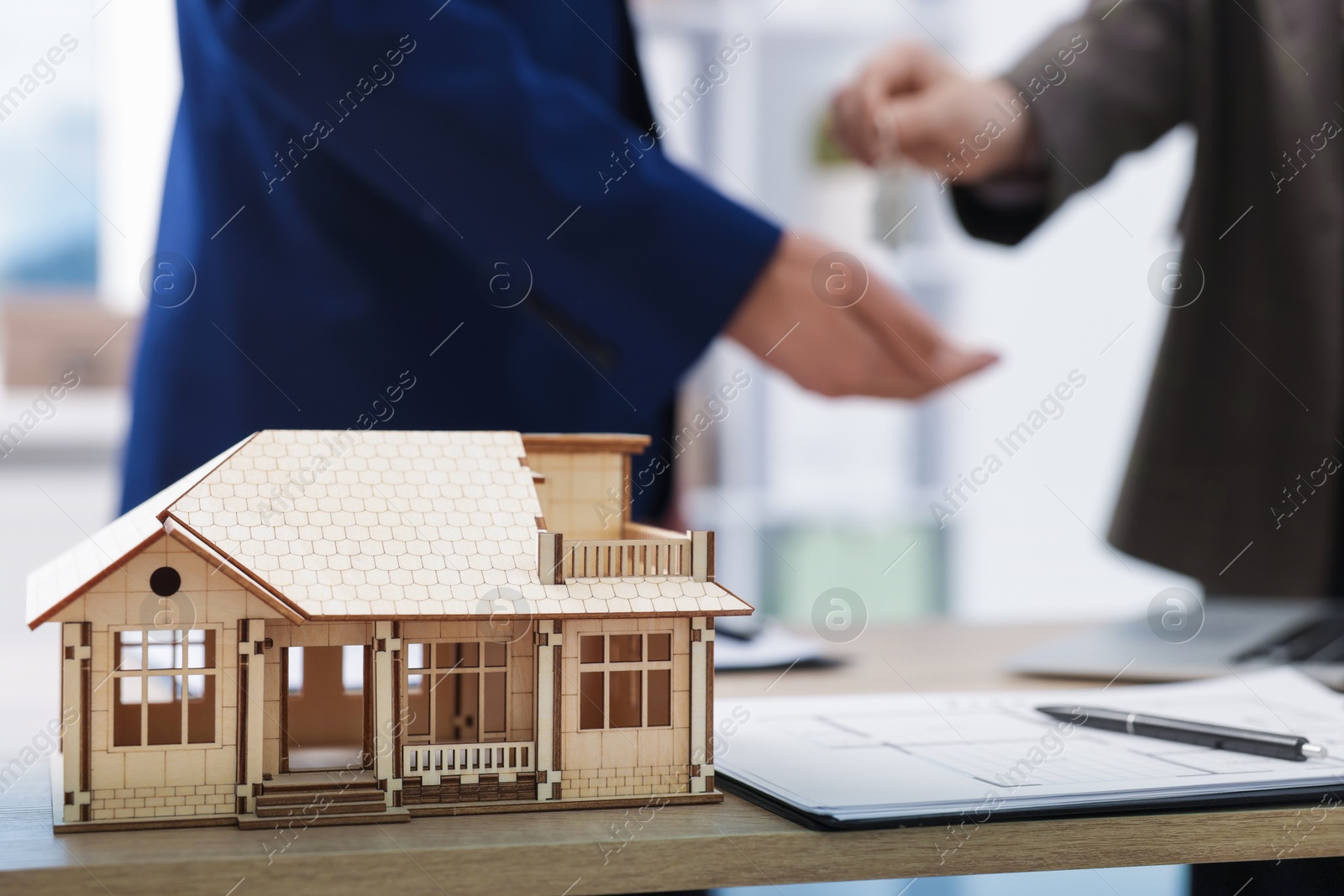 Photo of Real estate agent giving key to client at desk in office, focus on house model
