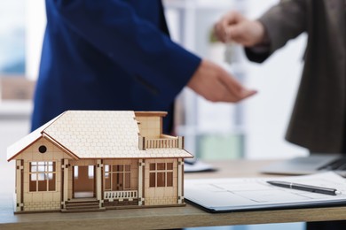 Photo of Real estate agent giving key to client at desk in office, focus on house model