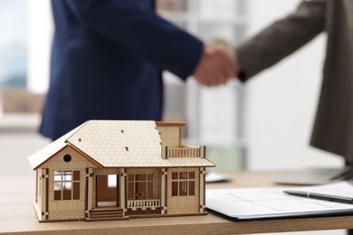 Photo of Real estate agent and client shaking hands at desk in office, focus on house model