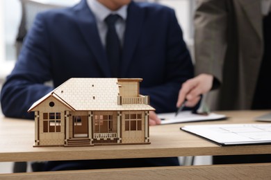 Photo of Real estate agent working with client at desk in office, focus on house model