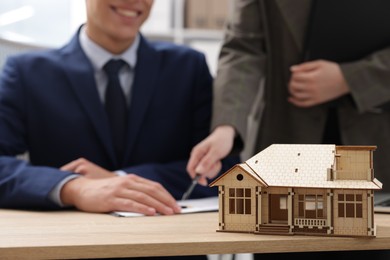 Photo of Real estate agent working with client at desk in office, focus on house model