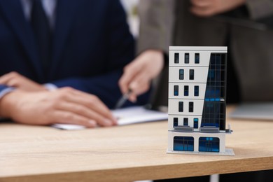 Photo of Real estate agent working with client at desk in office, focus on house model